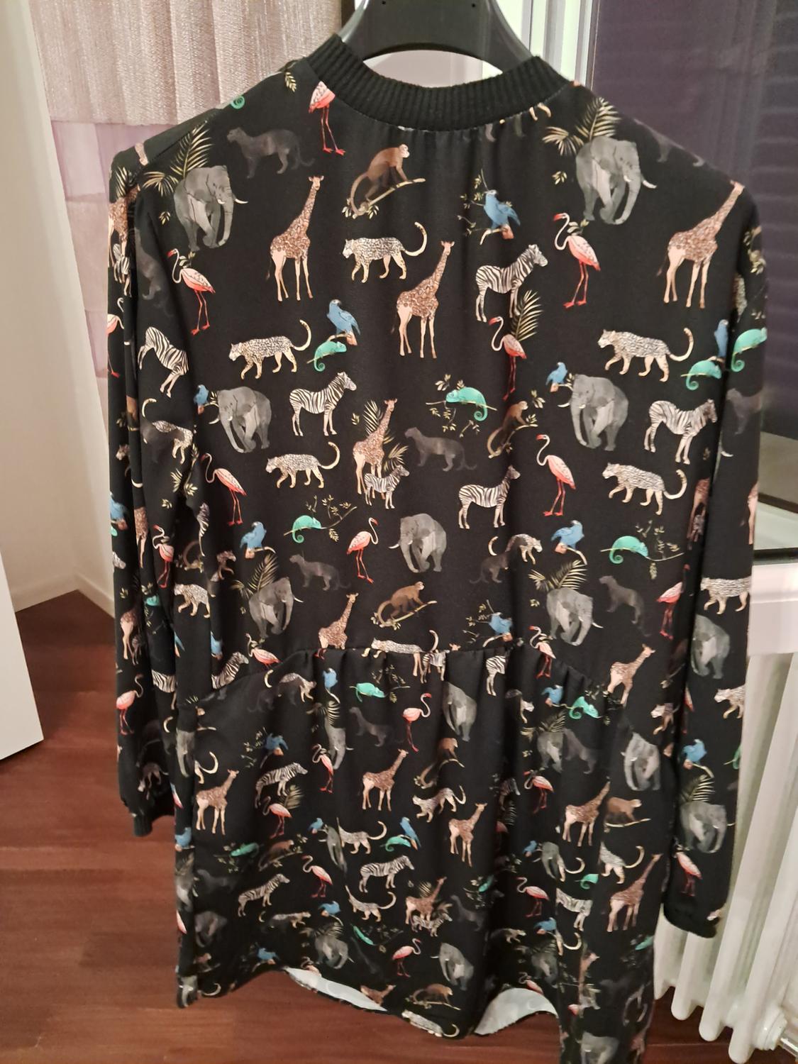 Long-sleeved black dress hanging indoors. Its elephant, giraffe and zebra print stands out, along with its ribbed collar.