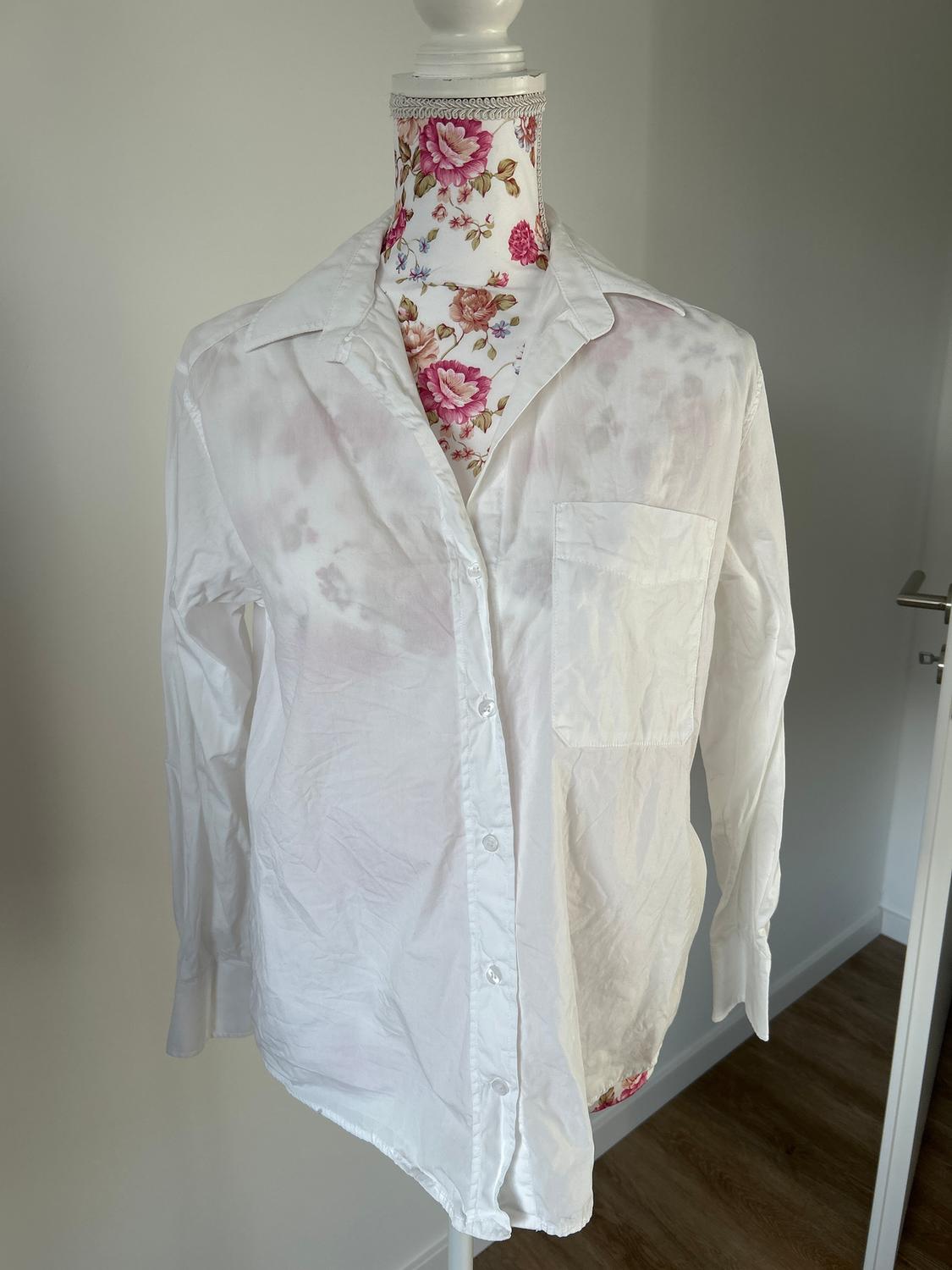 Mannequin with floral cover displays white button-down shirt with pocket in an indoor setting with wooden flooring.