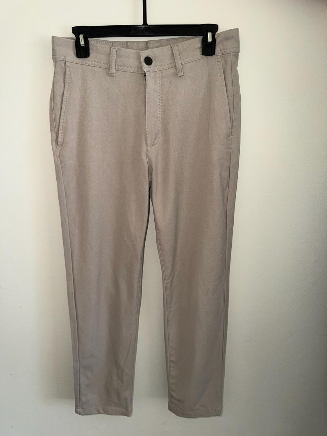 Light beige pants with side pockets and a button closure, hanging on a black hanger against a white background.