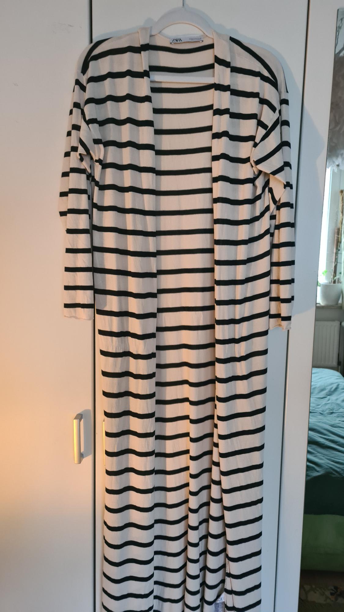 Long black and white striped cardigan hanging on a white hanger in front of a white wardrobe.