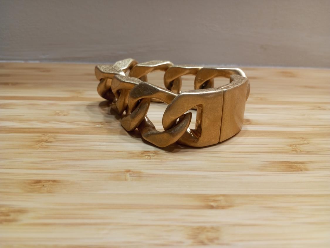 Large gold link bracelet on a light wooden surface. Neutral background and beige wall.