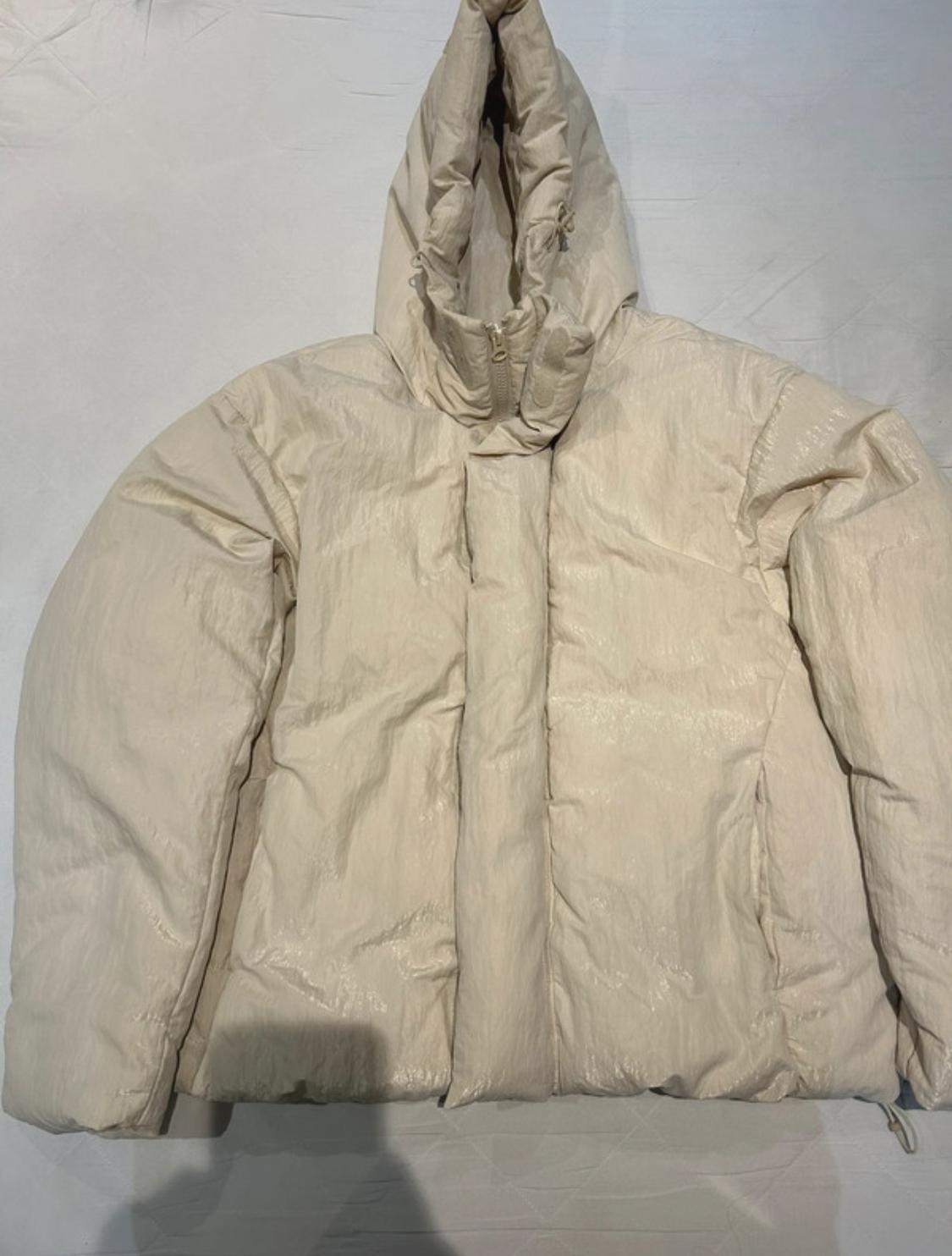 Beige padded jacket with hood on a white background. The texture is slightly shiny and it has a front fastening.
