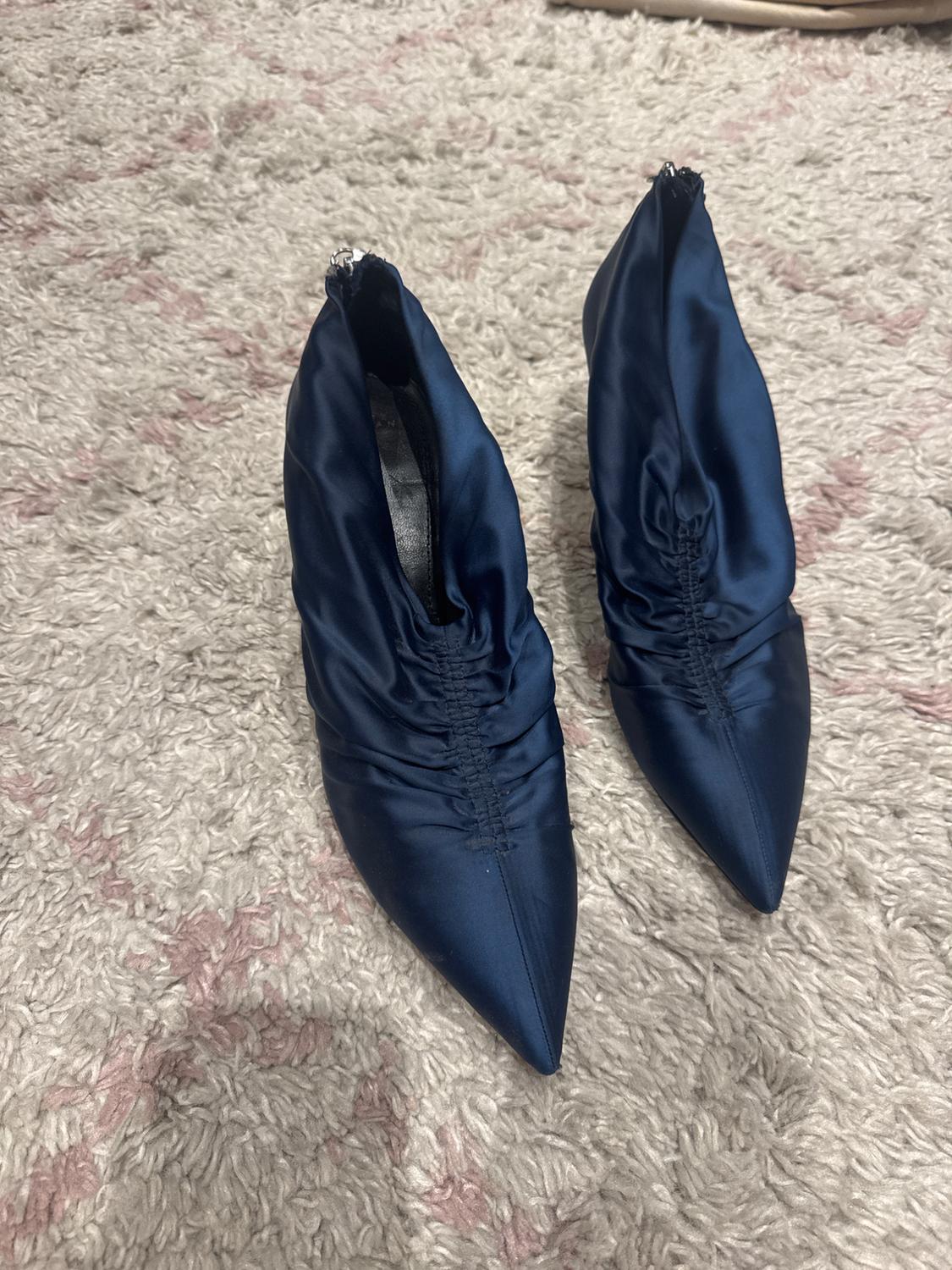 Navy blue pointed-toe ankle boots in satin fabric with ruched detailing on the instep, resting on a plush, light-coloured rug.