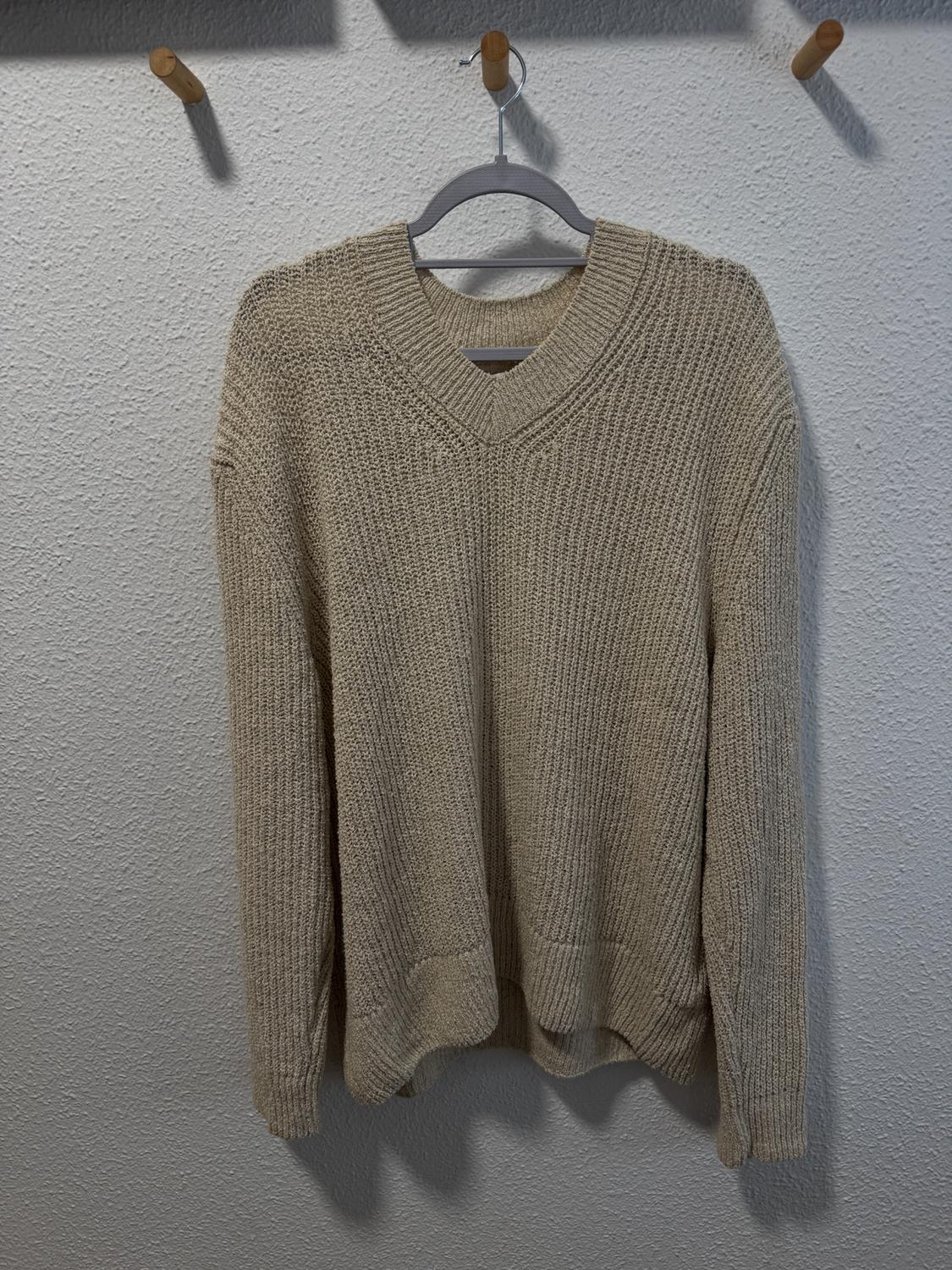 Beige knitted jumper hanging on a hanger against a textured white wall.