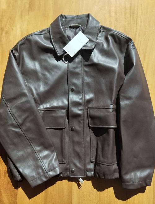 Brown faux leather jacket on a wooden background, with a white tag hanging from the collar.
