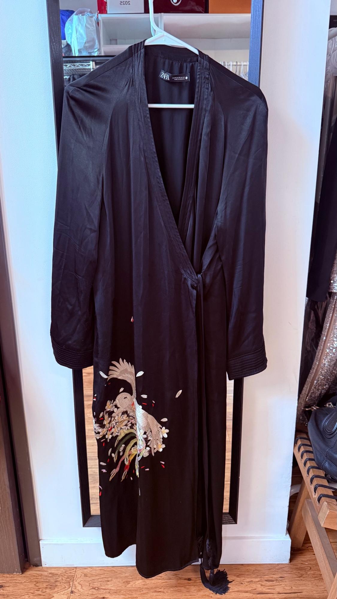 Black long-sleeve wrap dress with bird and floral embroidery hanging in front of a mirror. Text: ZARA, 2052.