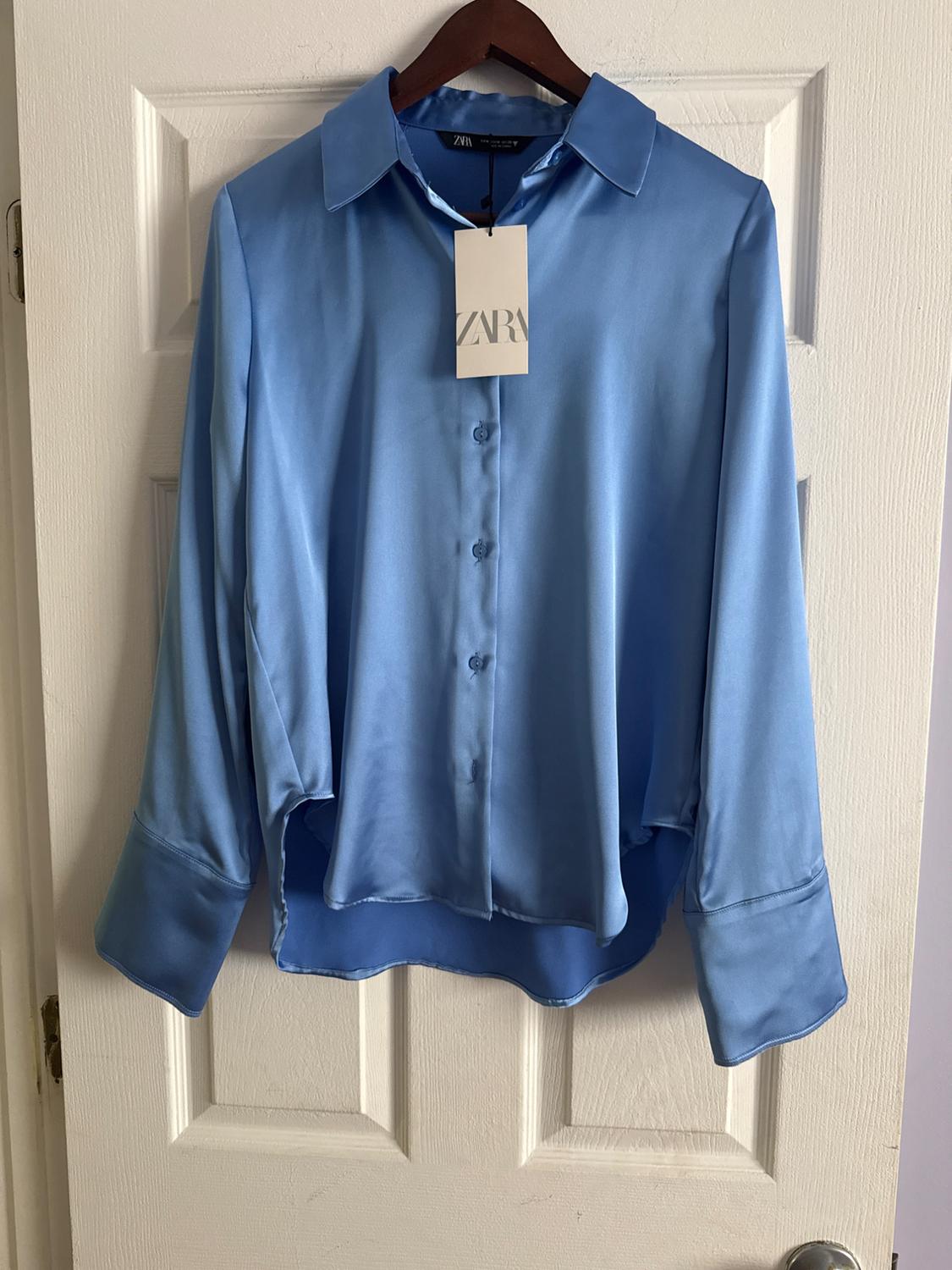 Blue satin shirt hanging on a white door, with Zara tag visible on the collar.