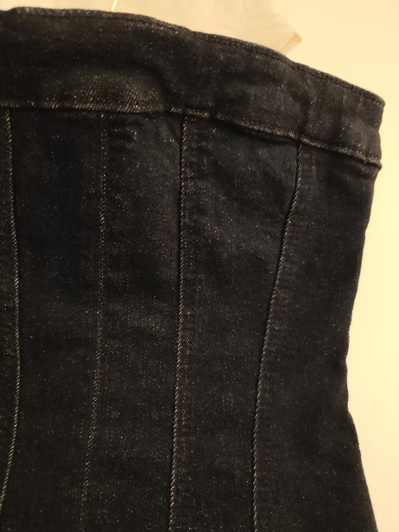 Close-up of a dark denim corset with visible stitching, hanging against a light background.