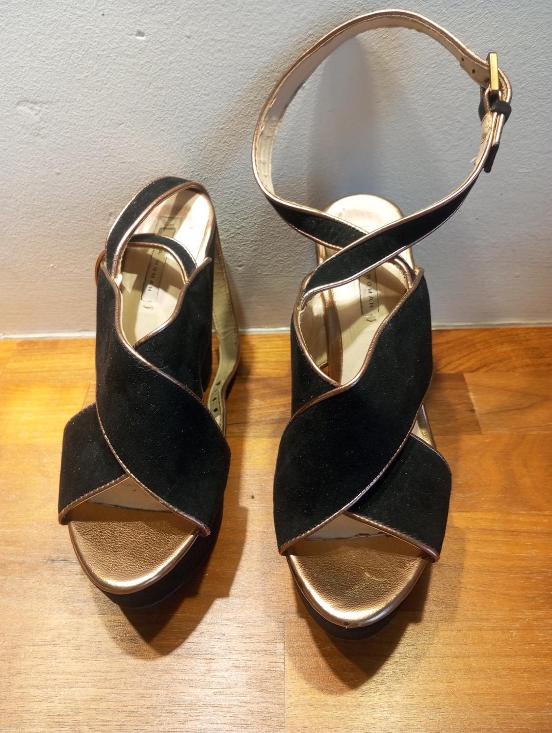 Black high-heeled sandals with crossed straps and a gold buckle, on a light wooden background.