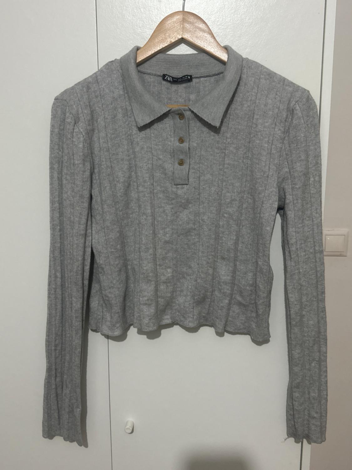 Grey long-sleeved shirt with collar and buttons, hanging on a wooden hanger over a white door.