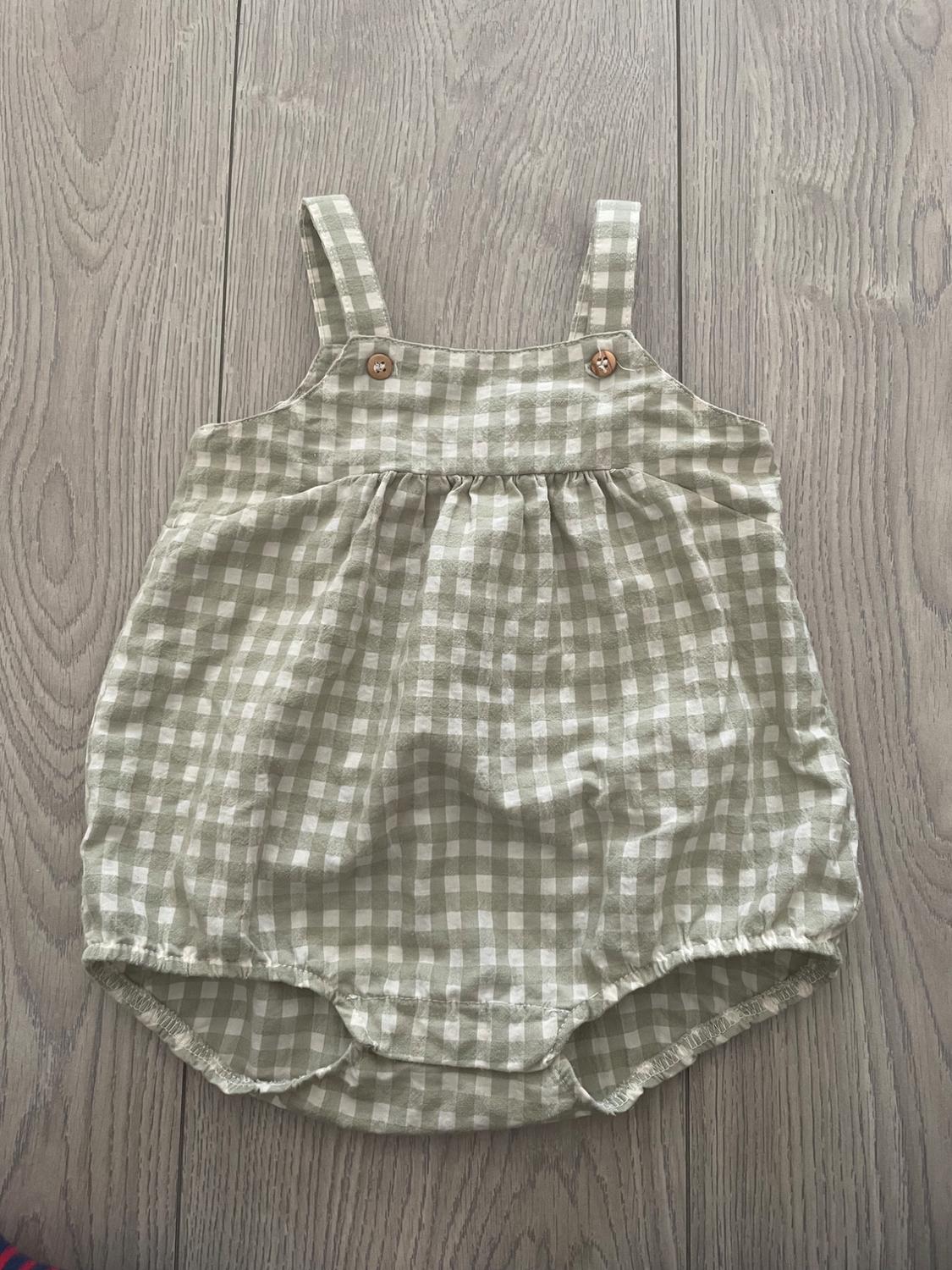 Baby romper with straps and wooden buttons, white and green check print, on a light wood background.