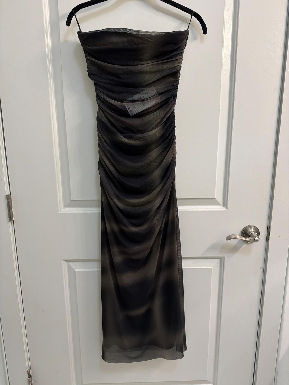 Strapless black dress with draping, hanging on a black hanger over a white door. Label visible in the center.