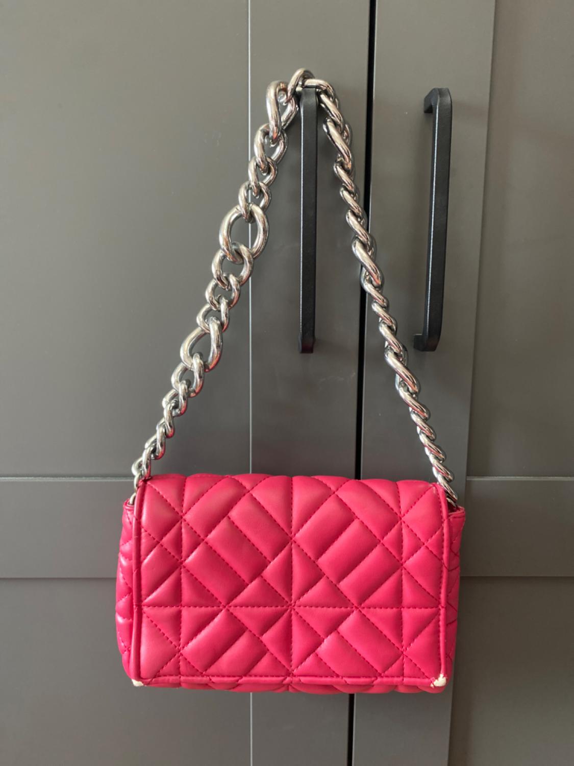 Pink quilted handbag with a metal chain, hanging from a dark grey wardrobe with black handles.