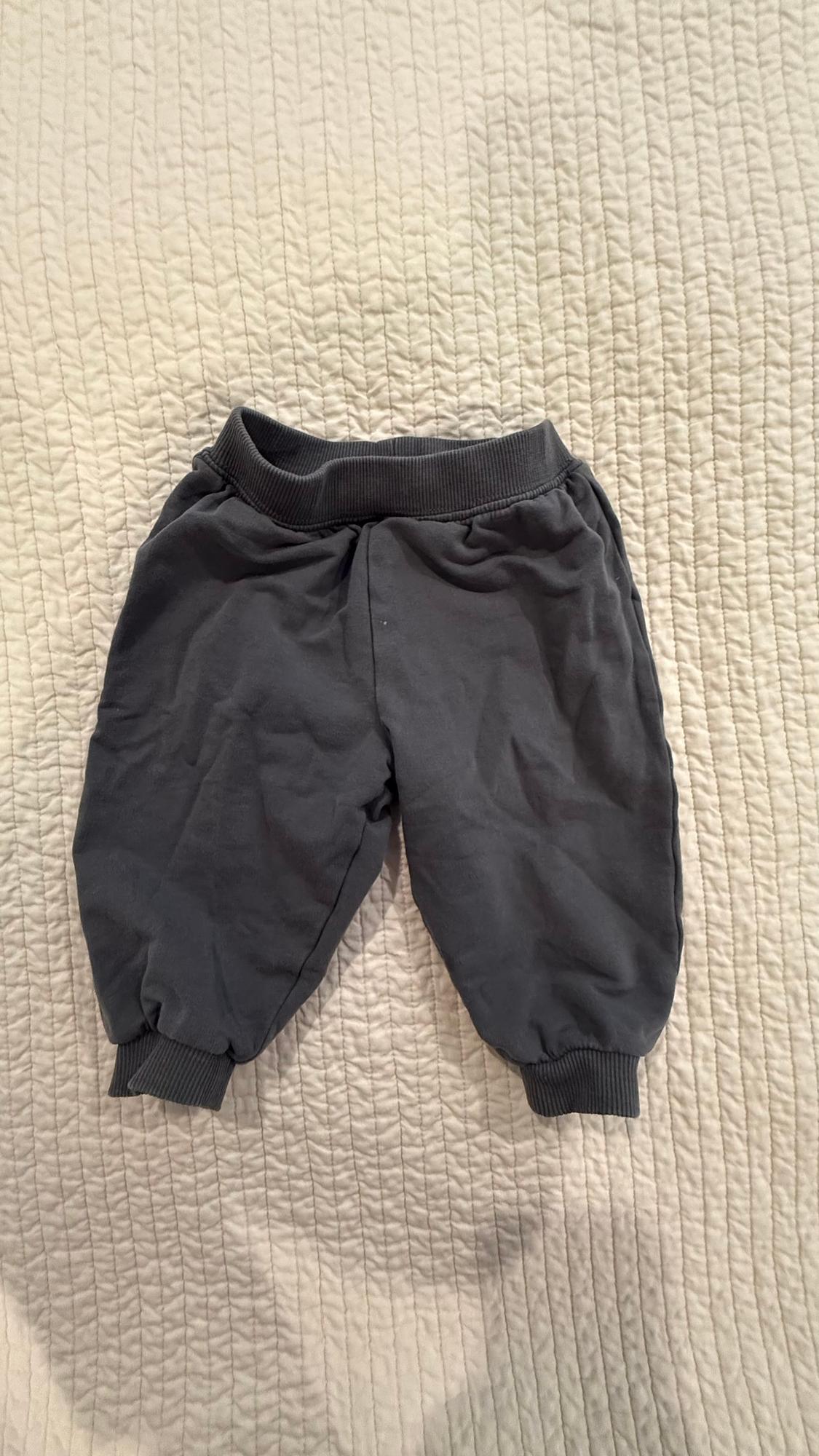 Grey baby joggers on a beige quilted bedspread.