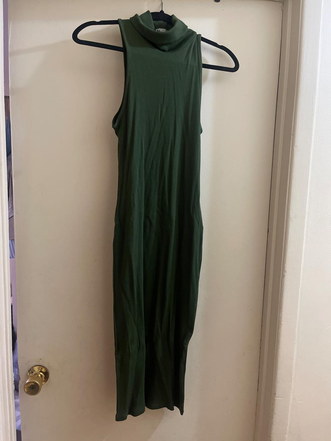 Dark green sleeveless maxi dress hanging on a black hanger over a white door.
