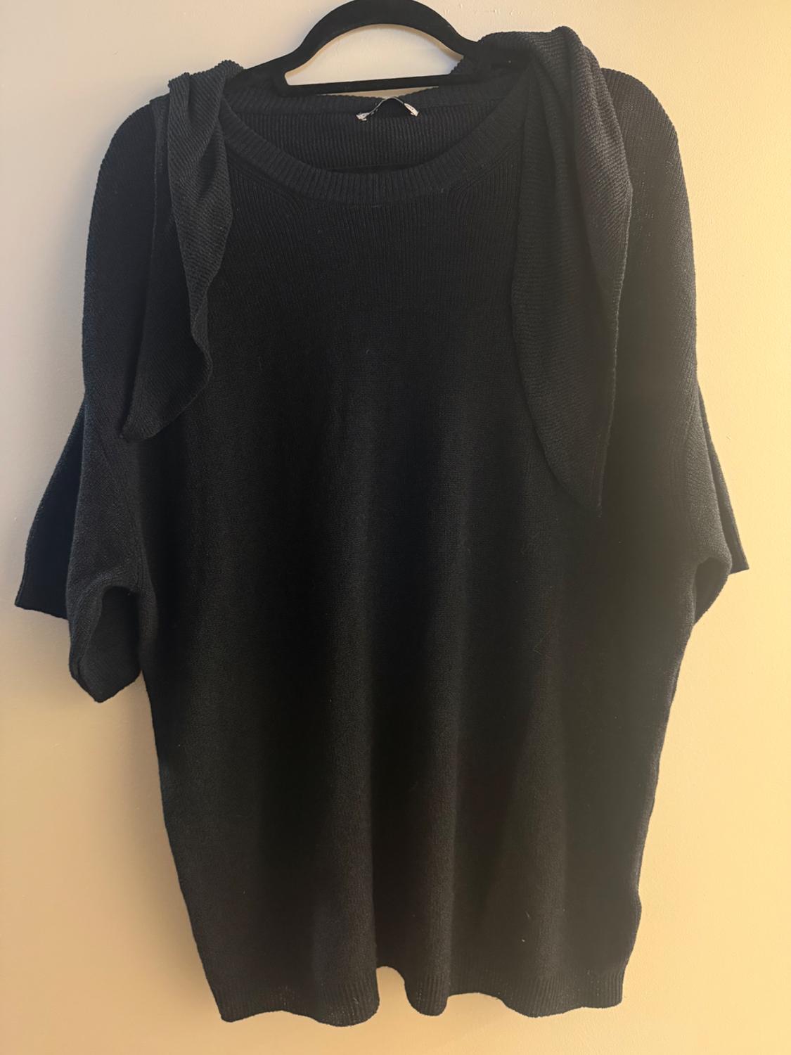 Black short-sleeved jumper hanging on a black hanger against a beige wall.