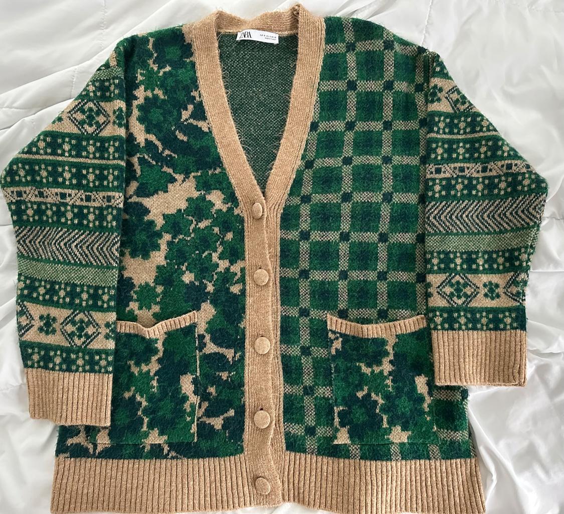 Knitted cardigan with geometric and floral print in green and beige, with buttons and front pockets, on a white background.