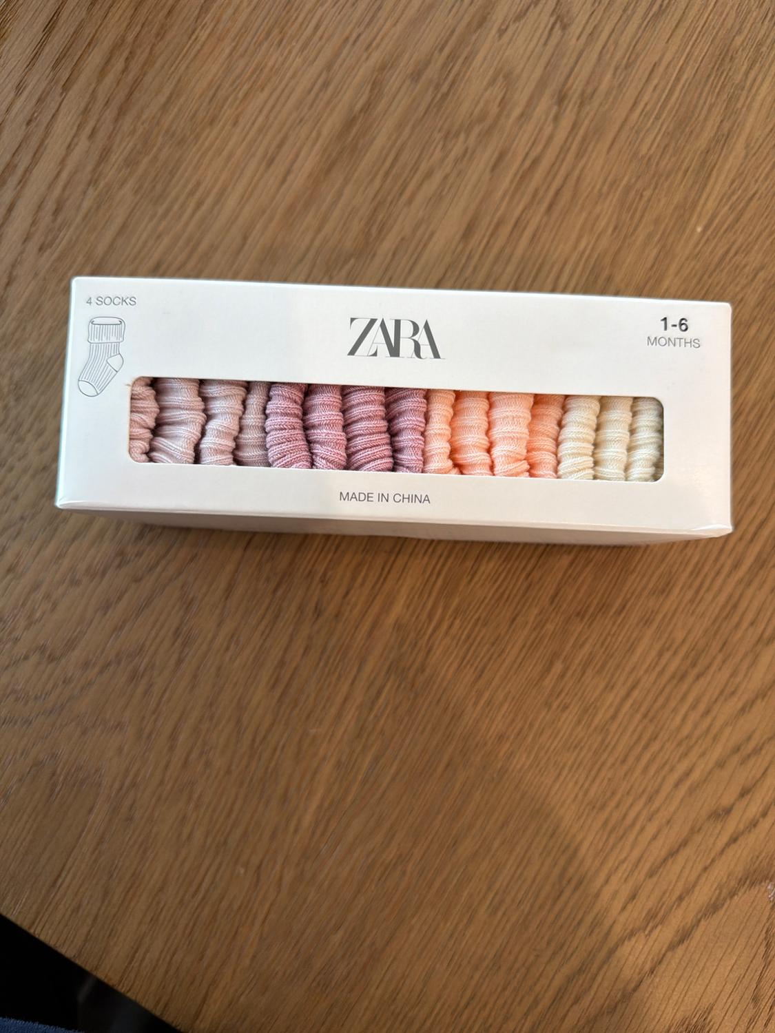 Box of baby socks for 1-6 months, Zara brand, in pastel shades. Visible text: "4 socks", "Zara", "Made in China".