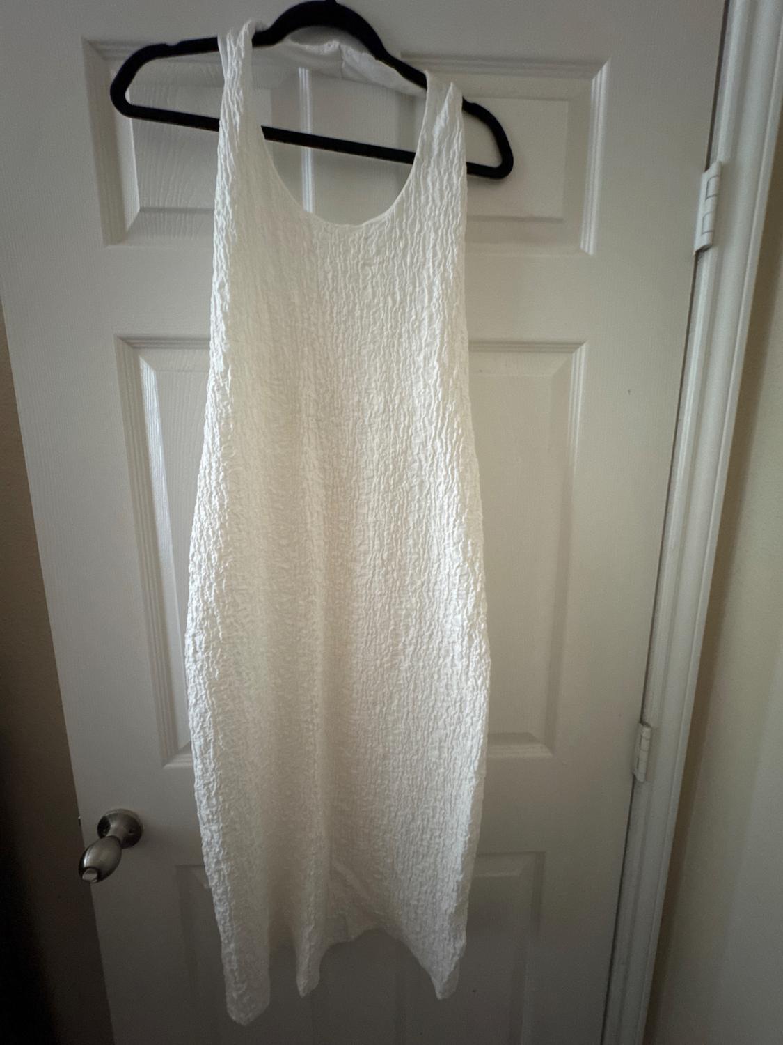 Sleeveless white dress with crinkled texture hanging on a black hanger over a white door.