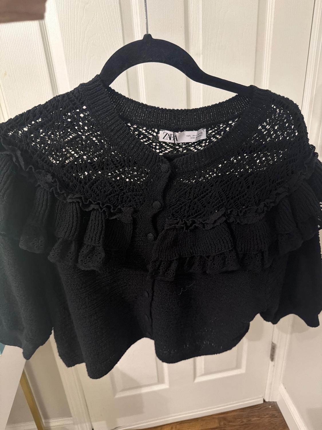 Black knit jacket with lace and ruffle details, hanging on a black hanger. Visible tag with "ZARA" text.
