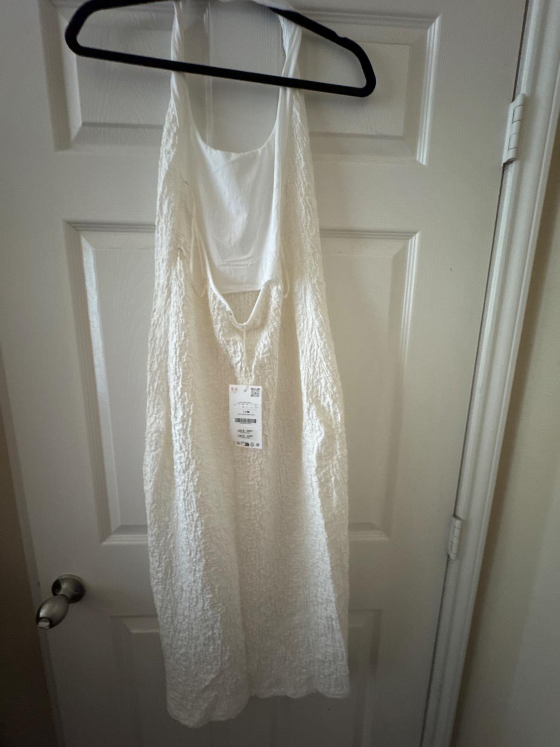 Wrinkled white fabric dress hanging on a black hanger over a white door. Label visible in the center of the dress.