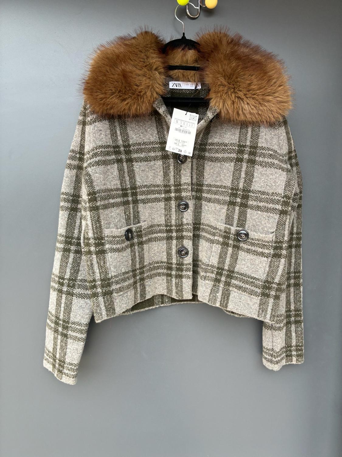 Grey and green checked jacket with a brown fur collar. Buttoned, hanging on a hanger against a grey background. Label with ZARA text visible.