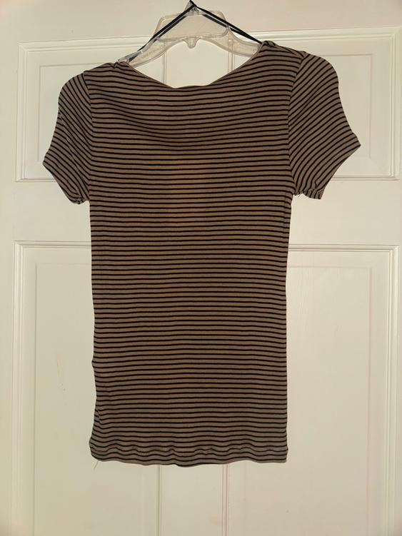 Black and brown striped t-shirt hanging on a clear hanger over a white door.