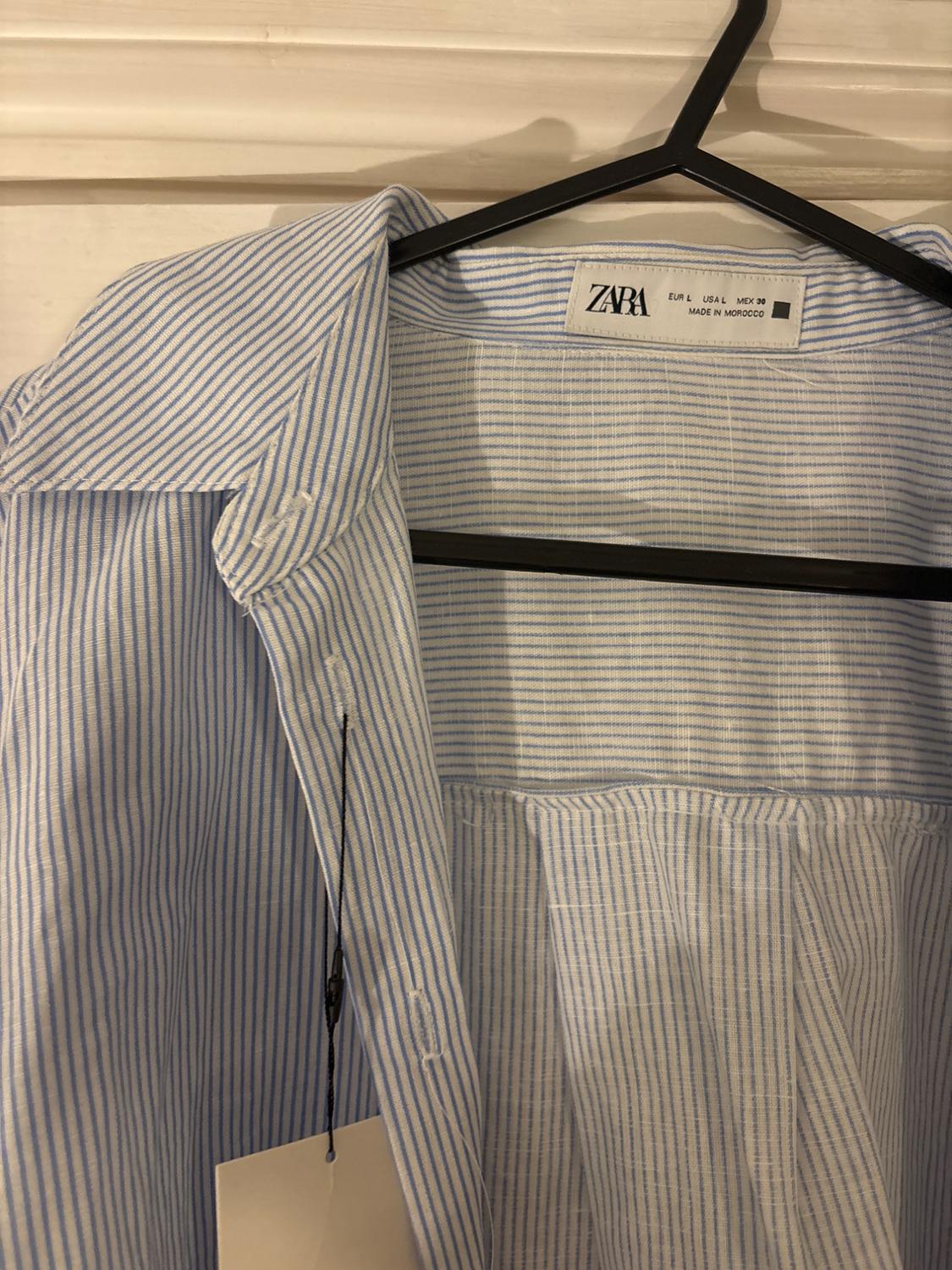 Blue and white striped shirt hanging on a black hanger. Visible label: "ZARA, EUR L, USA L, MEX 30, MADE IN MOROCCO".