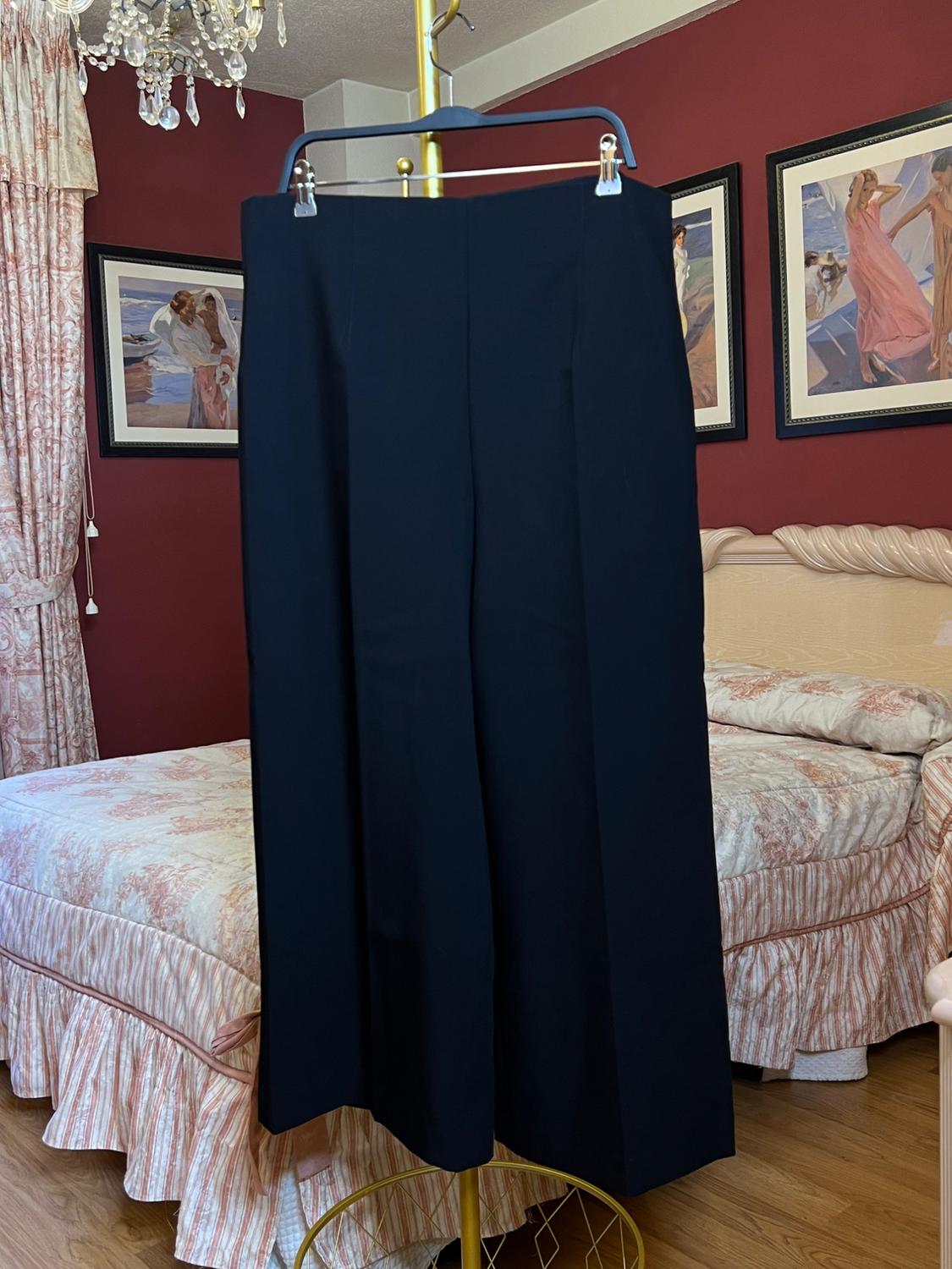 Black trousers hanging on a gold hanger in a bedroom with red walls, a bed with a floral bedspread, and pictures on the wall.