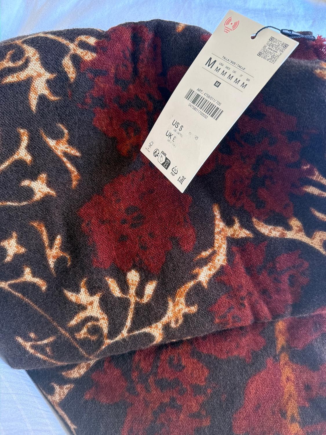 Fabric with a floral print in red and brown tones, visible label with size M and price US$ 20, on a white background.