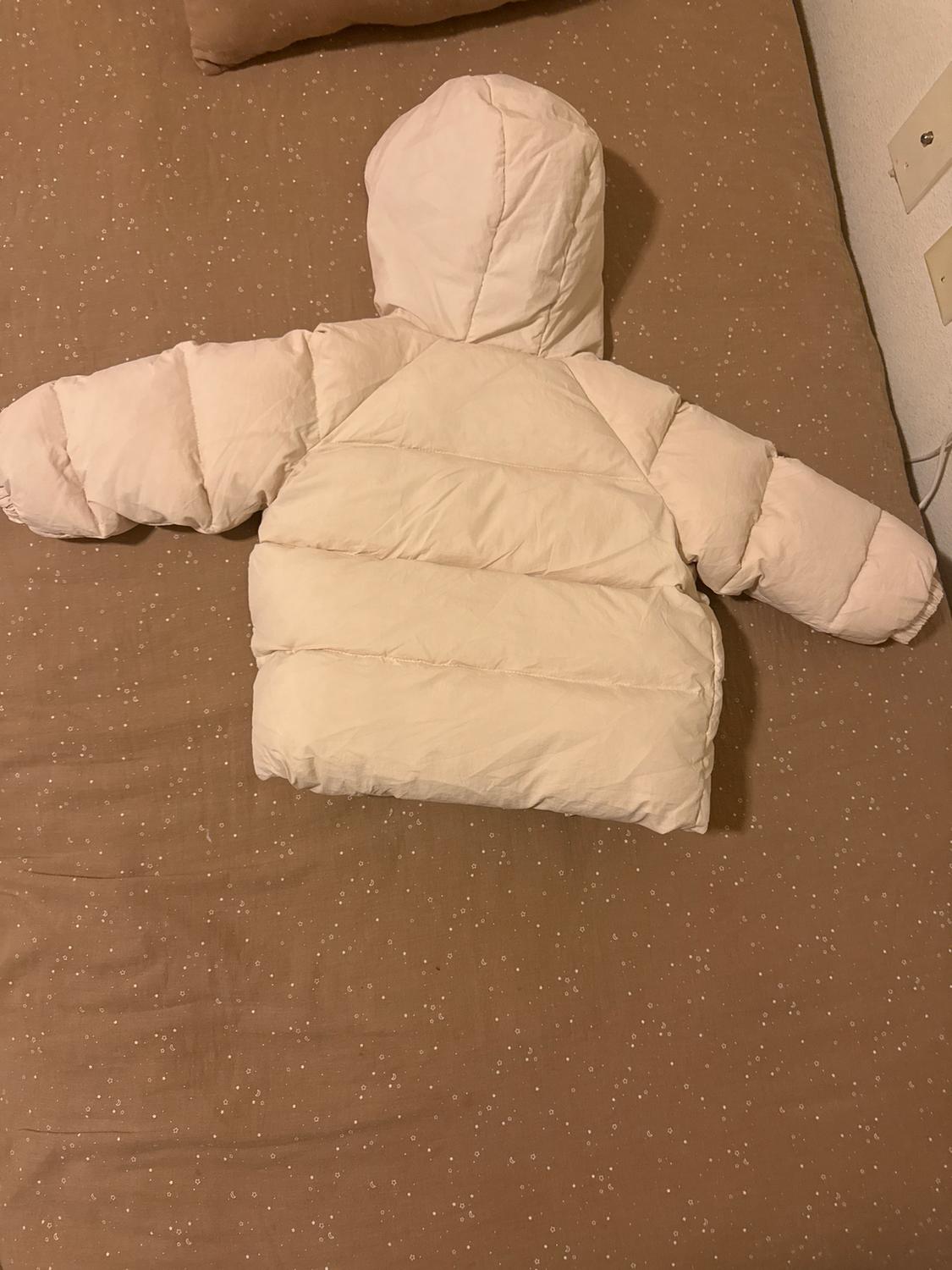Beige padded jacket with a hood, laid out on a brown bed with small white dots.