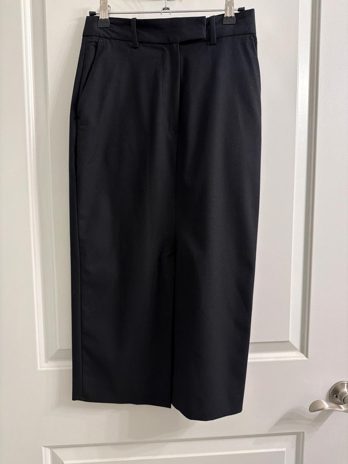 Black pants hanging on a hanger over a white door. Simple design with side pockets and belt loops.