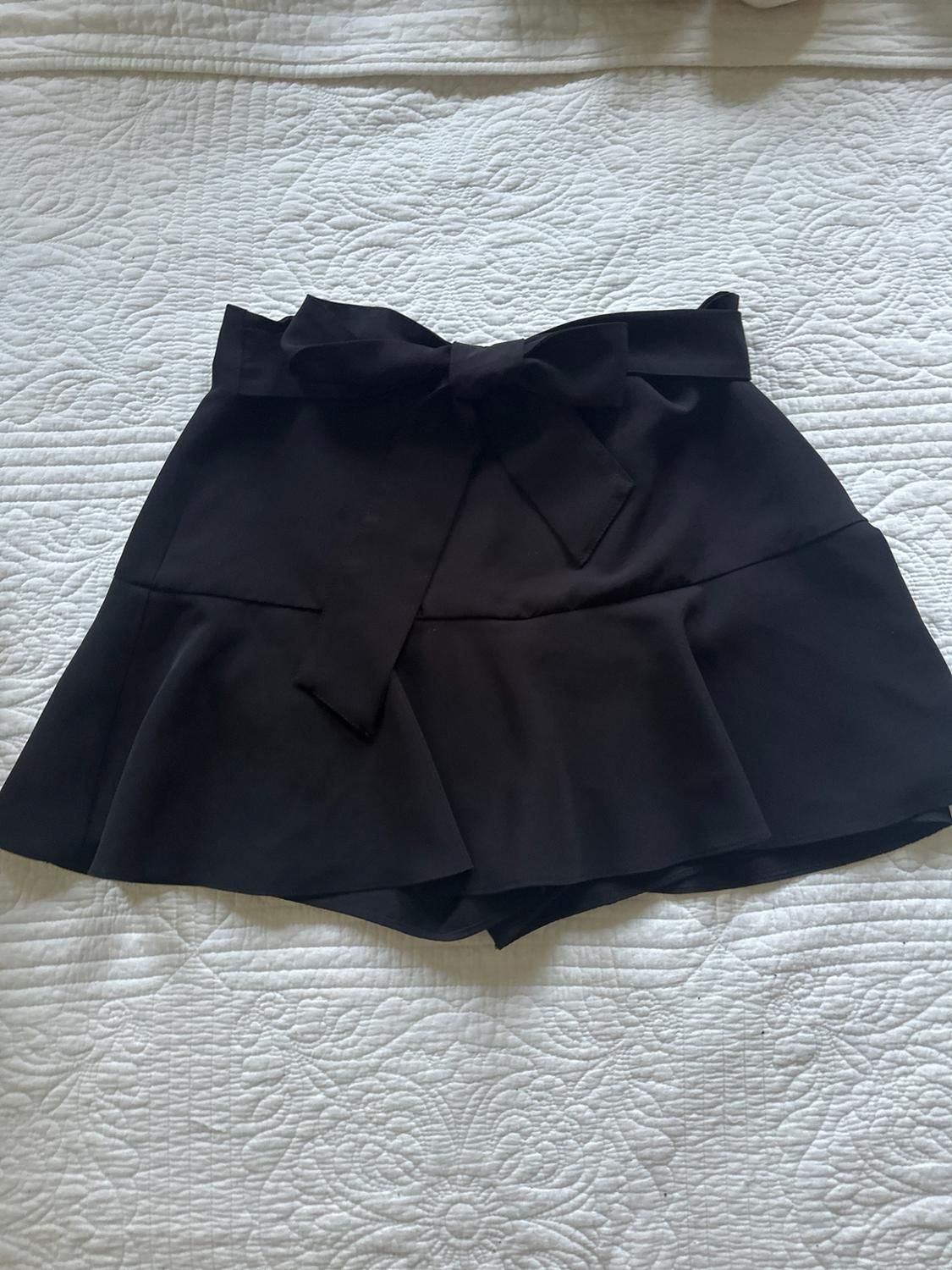 Black skirt with a bow at the waist and a flared hem, on a textured white bedspread.