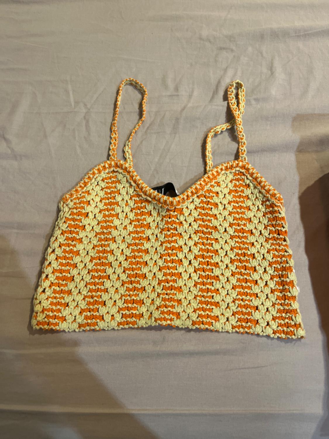 Crochet top in shades of orange and cream with thin straps, on a beige surface. Summery and casual design.