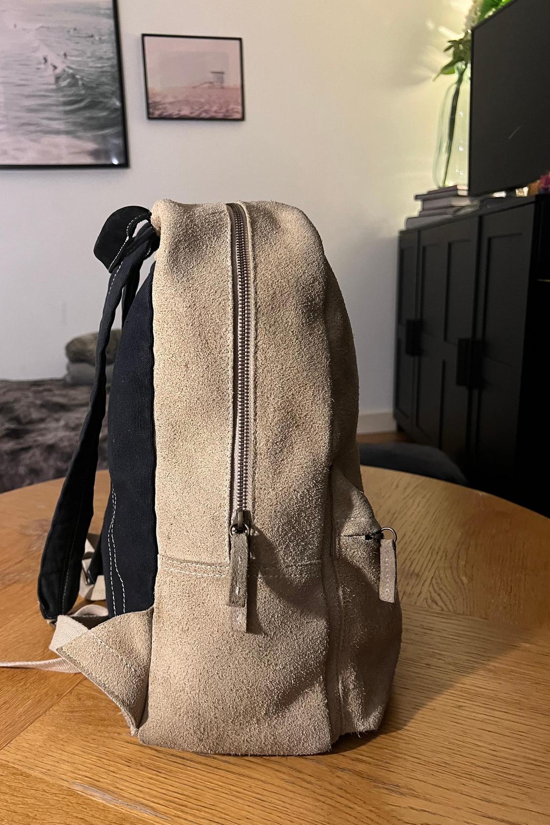 Side view of a beige rucksack with a zip and black details.