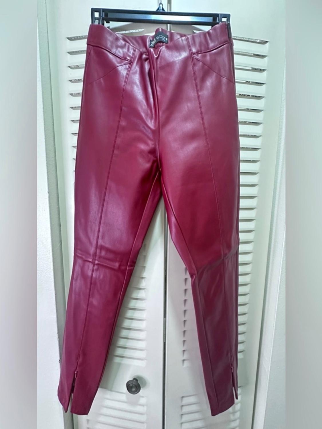 Red leather trousers hanging on a hanger in front of a white door with blinds.