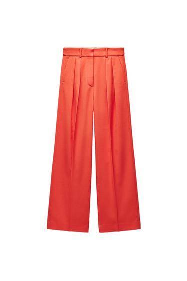 Front view of orange pleated pants with side pockets.