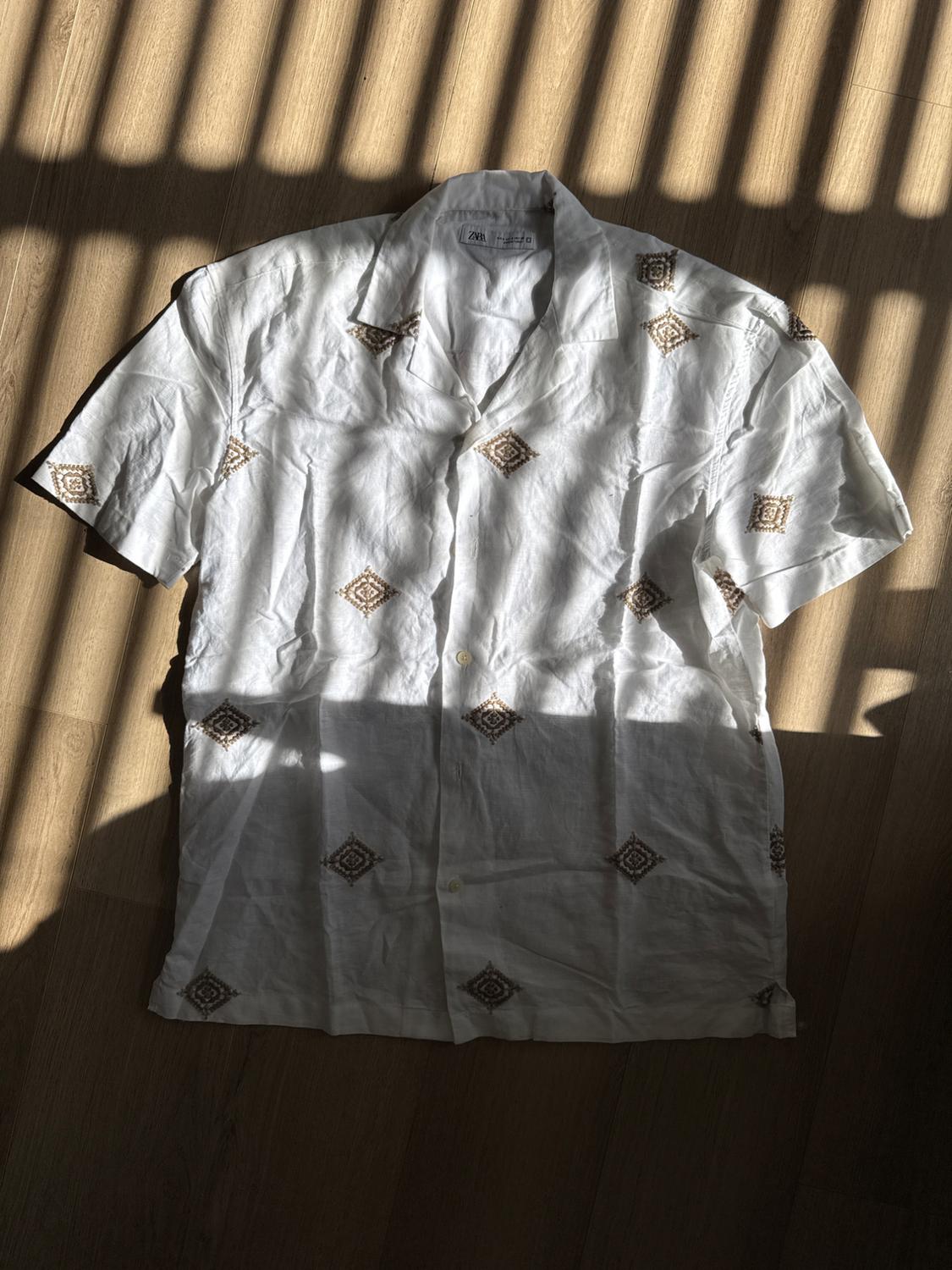 White shirt with brown diamond pattern on a wooden floor. Light creates linear shadows in the background.