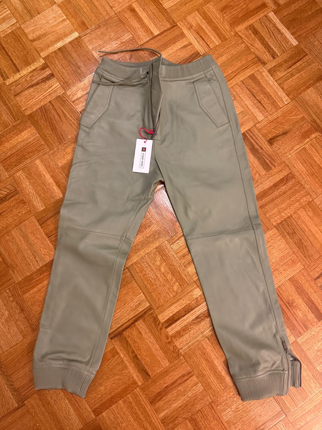 Khaki jogger trousers with a white label and red drawstring, on a light brown parquet floor.