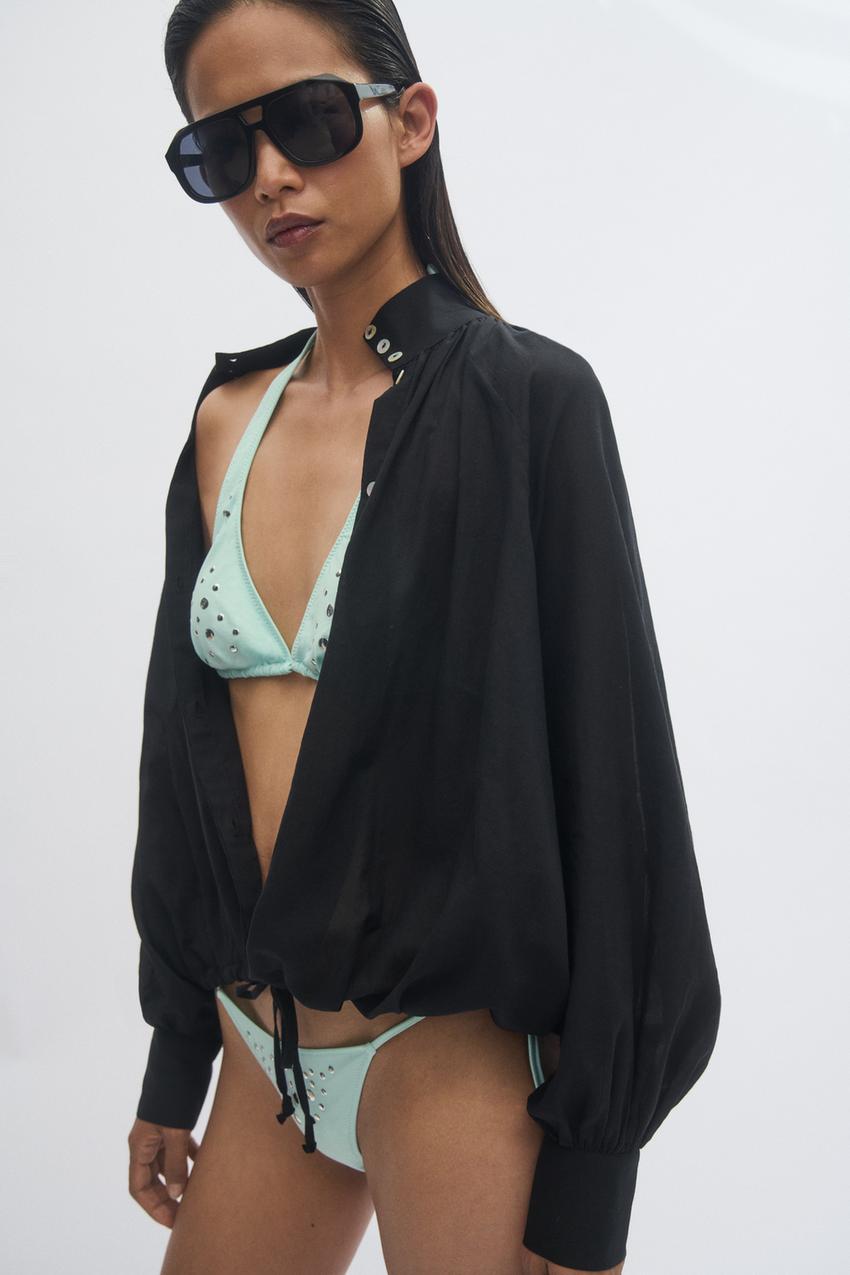 Set of an open black button-down shirt with long puff sleeves and a drawstring hem, a light blue bikini with appliqu&eacute;s, and sunglasses.
