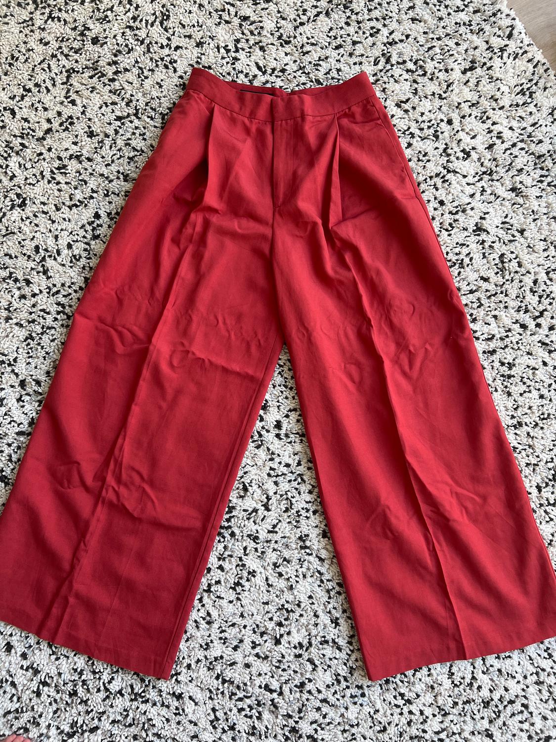 Red, wide-leg trousers with pleats, placed on a black and white textured rug.