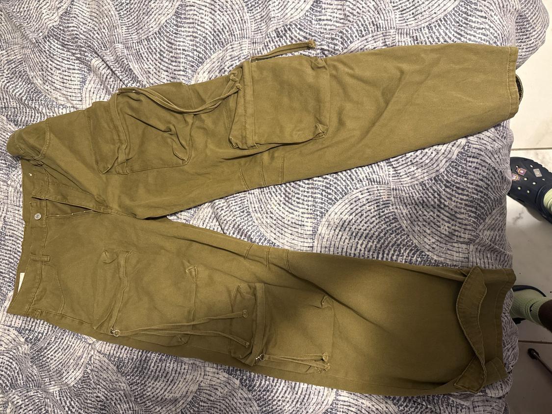 Olive green cargo pants with pockets and drawstrings, laid out on a sheet with a blue-and-white geometric pattern.