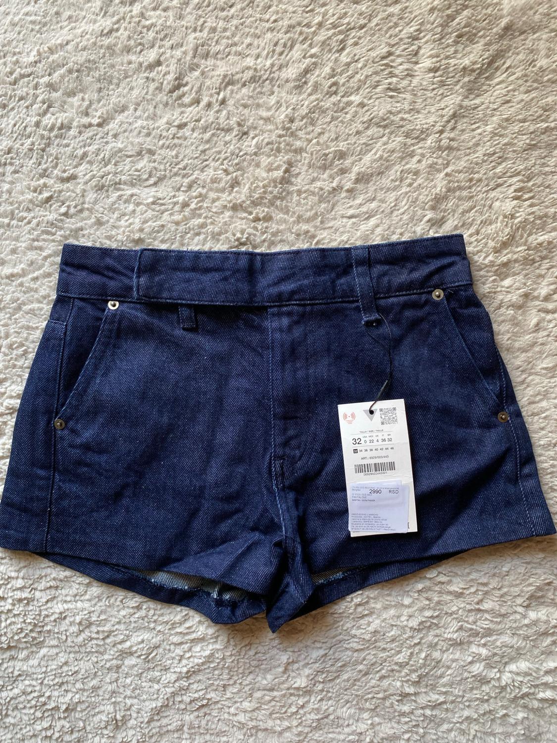 Dark blue denim shorts with pockets on a white carpet. Label with text: 32, ART: 6929/003/443, 2990 RSD.