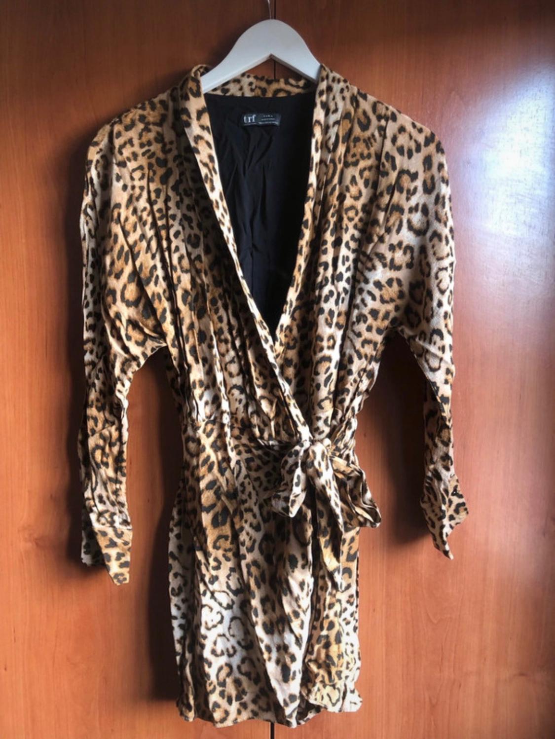 Short animal print dress hanging on a white hanger against a wooden background. "trf" label visible on the collar.