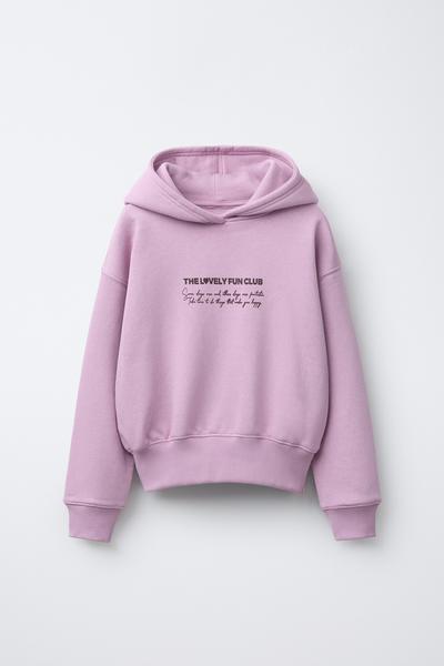 Vorderansicht eines rosafarbenen Hoodies mit Kapuze und dem Text „THE LOVELY FUN CLUB“ auf der Brust. Gerippte Bündchen und Saum.
