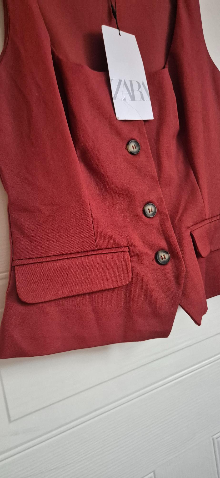 Red waistcoat with front buttons, flap pockets and a white label with the text ZARA, on a white background.