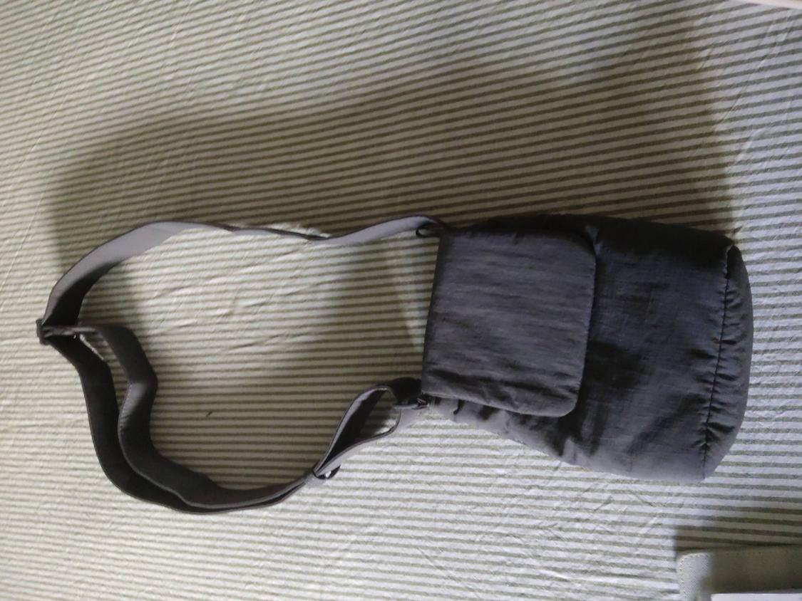 Dark grey casual shoulder bag with a flap and long strap, resting on a fabric surface with light horizontal stripes.