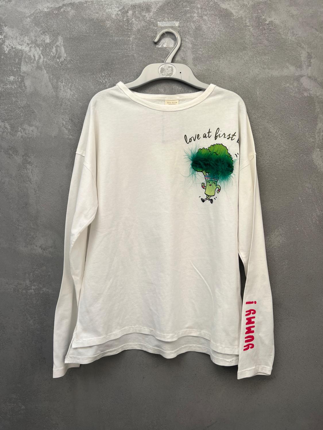 White long-sleeved t-shirt with broccoli illustration and "love at first" text. Sleeve with red "I AMMR" text. Grey background.