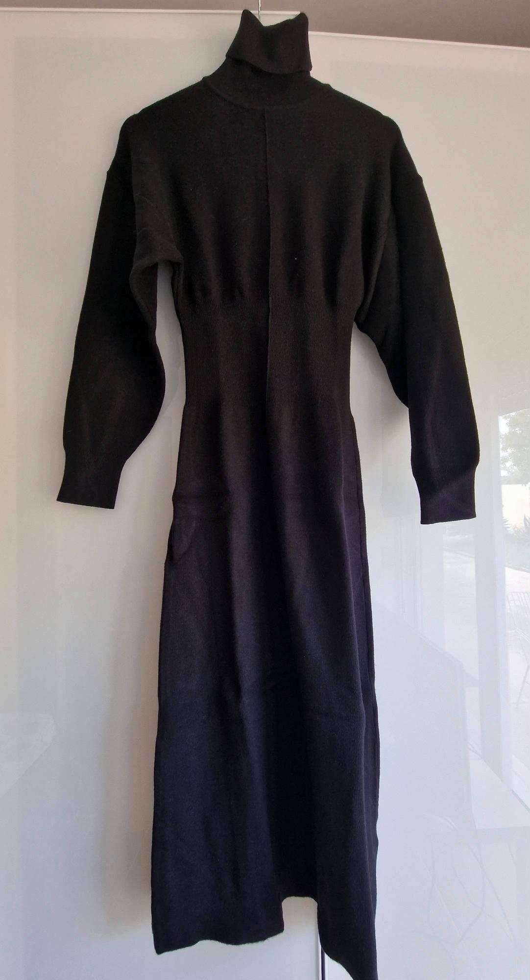 Long black knitted roll-neck maxi dress with long sleeves and a ribbed waist, hanging against a white background.