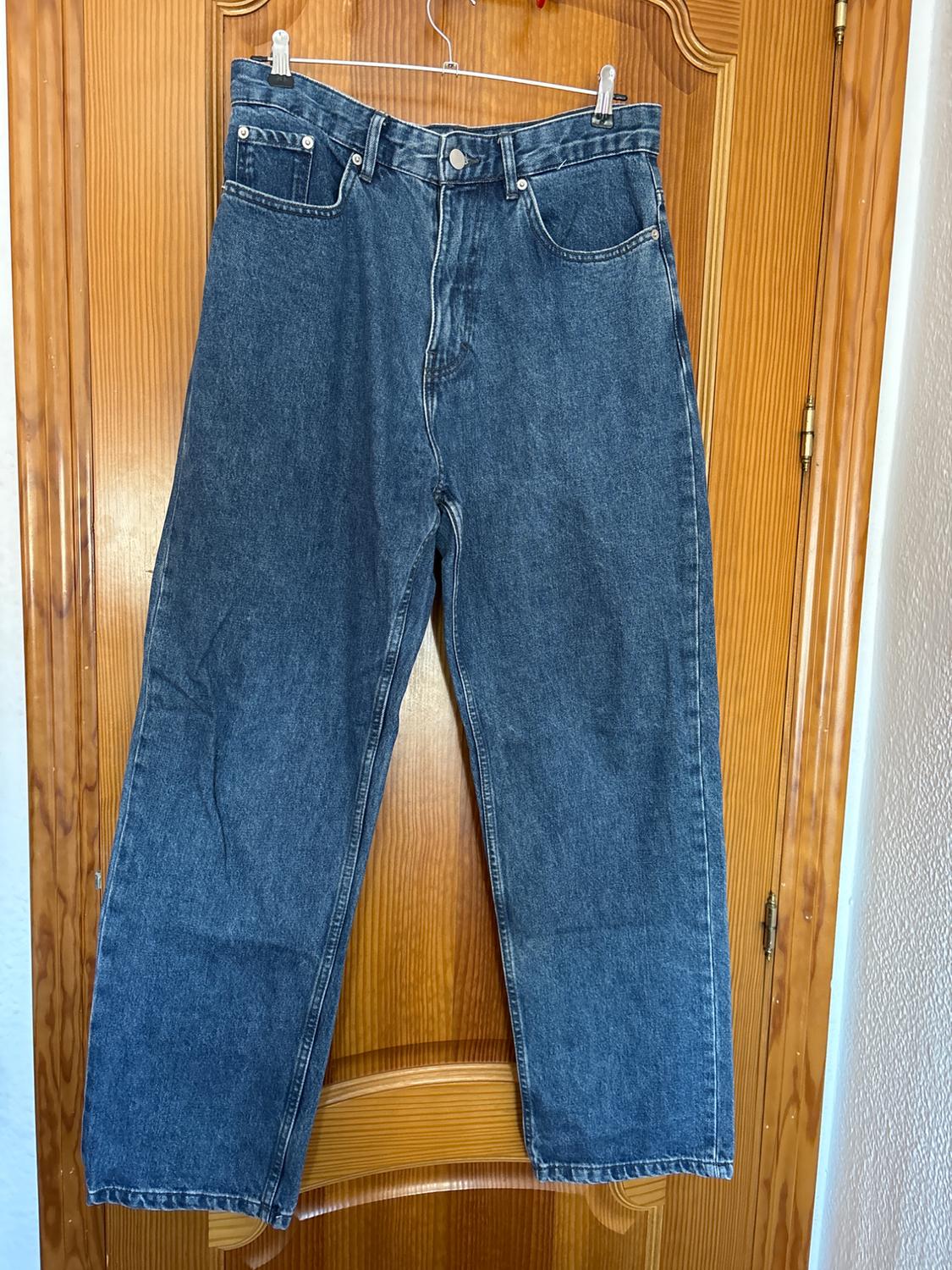 Blue jeans hanging on a hanger over a wooden door. Classic five-pocket design with button fastening.